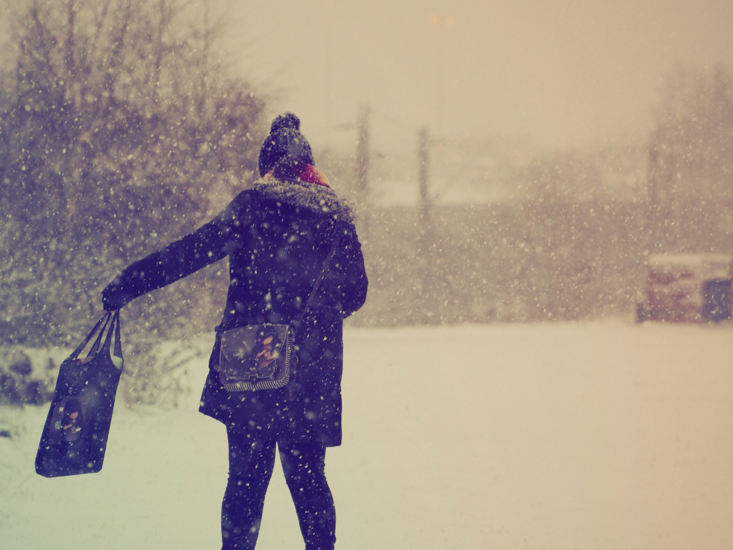 Shot from behind a woman as she walks through the snow as it falls.