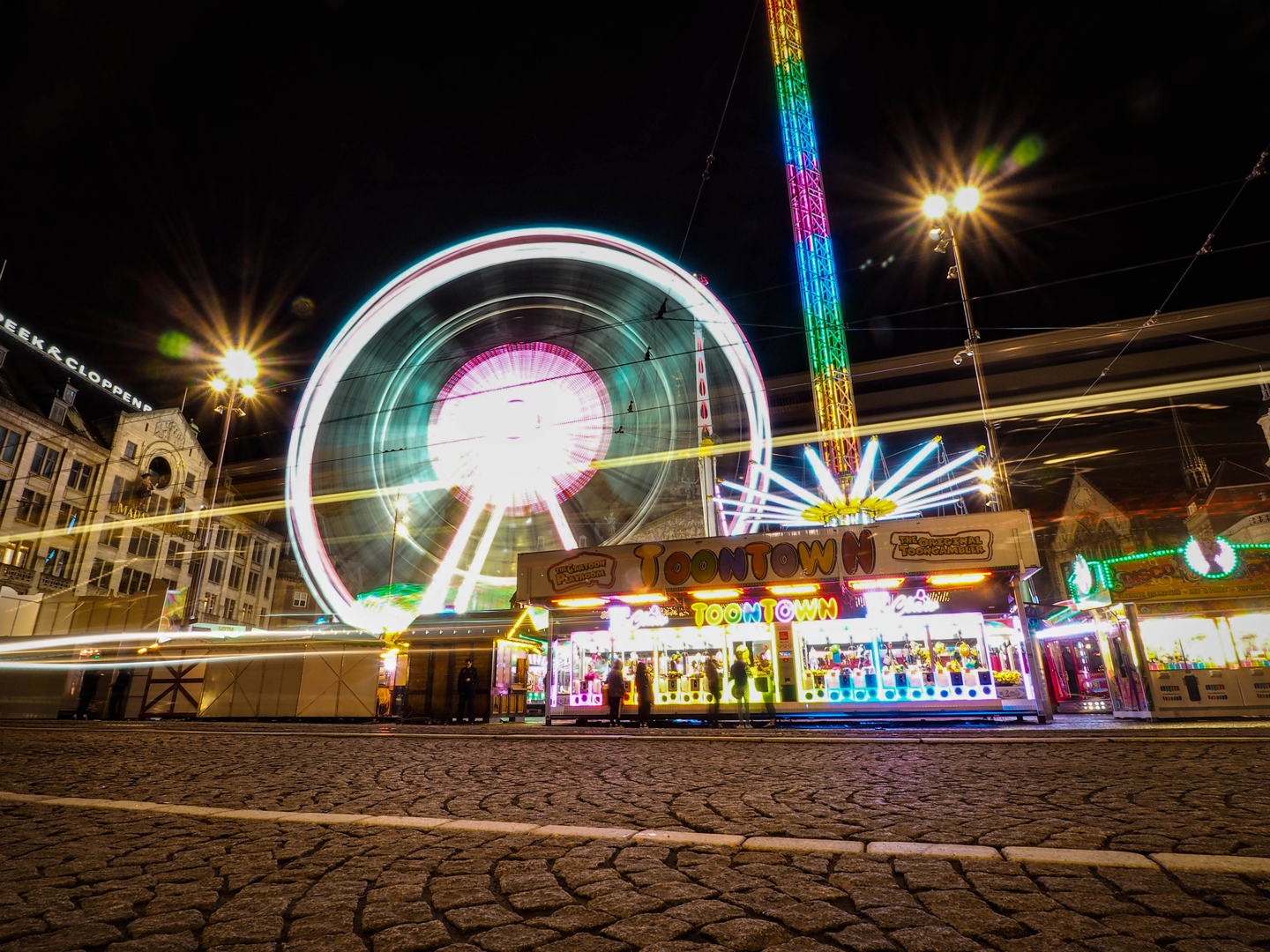 Long-exposure night shot of a carnival with Ferris wheel and colorful lights.
