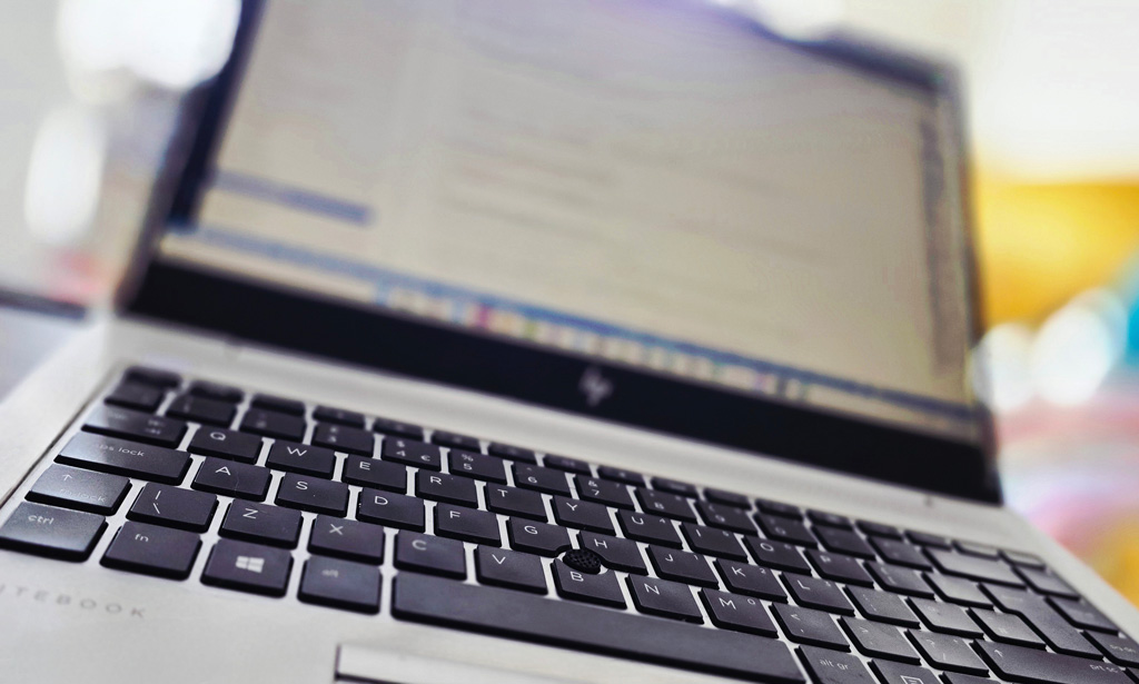 A close-up photo of a laptop keyboard and screen, with the focus on the keys and a blurred code editor open on the display.