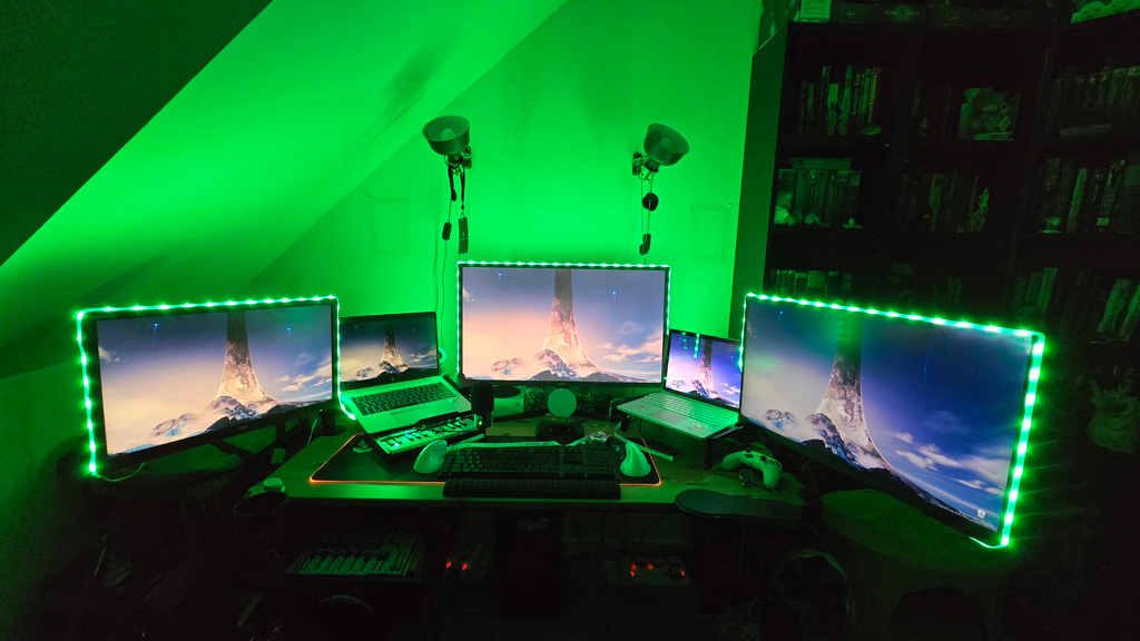 A multi-monitor computer setup with green lighting, showing Halo ringworld images on all screens.
