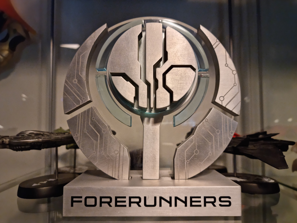 A metallic Halo Forerunners emblem with circuit-like patterns, displayed on a stand labeled ‘Forerunners.’